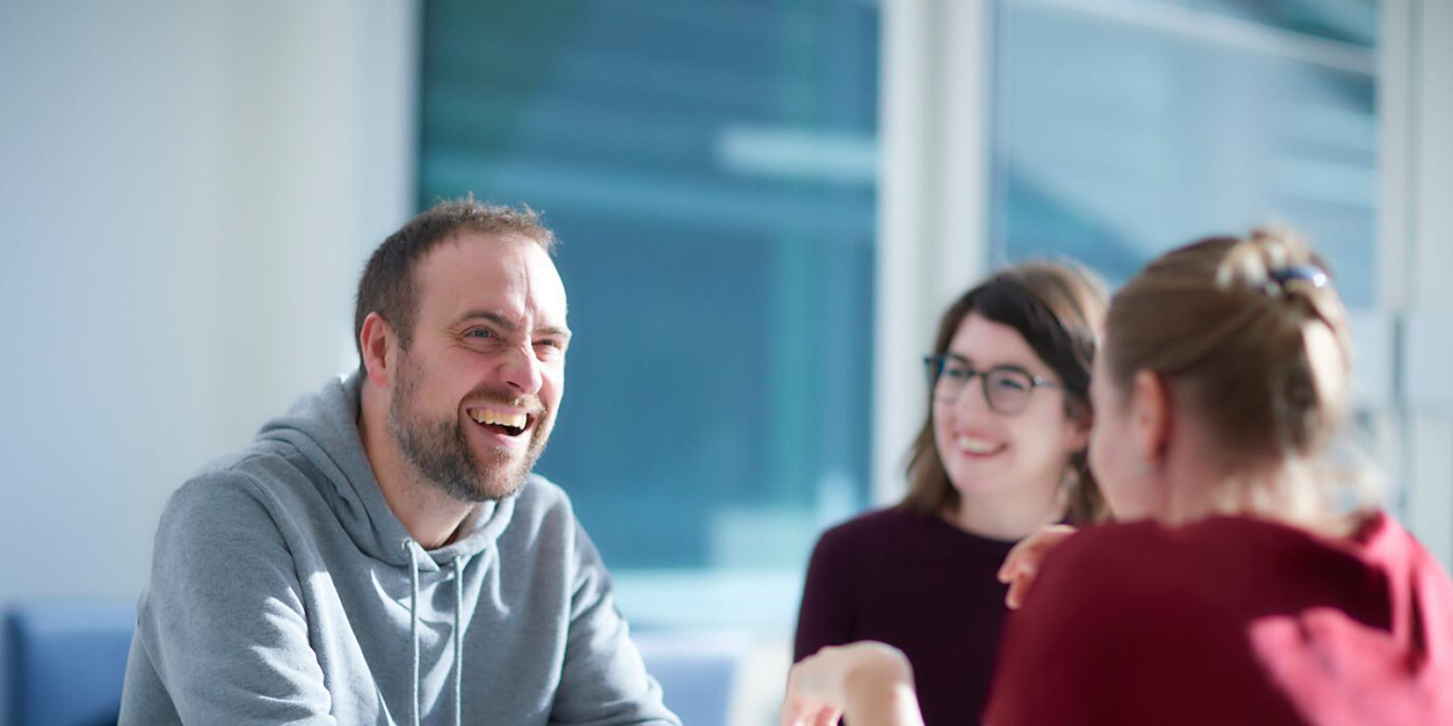 Man laughing with two women in meeting